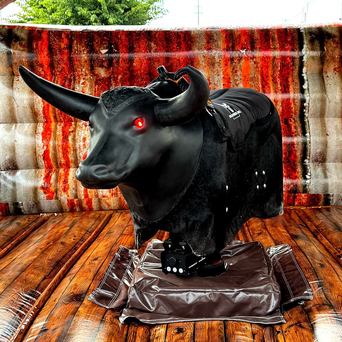 Exclusive package — all-black mechanical bull with black horns and red LED eyes on a wood-print floor